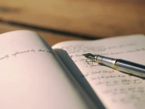 Quaderno aperto con un testo scritto a mano e penna stilografica