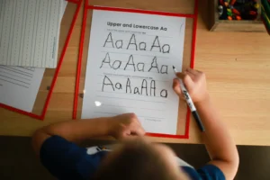 Bambino visto dall'alto che si esercita a scrivere su una scheda la lettera a