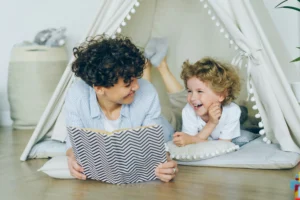 Madre legge un libro ad alta voce al figlio, entrambi sono sdraiati sotto una tenda.