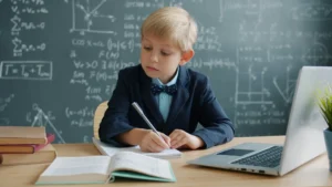 bambino seduto a una scrivania che scrive su un quaderno, sullo sfondo una lavagna con operazioni matematiche