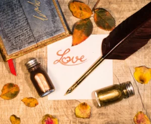 Un foglio con la scritta Love, una penna d'oca con pennino, due boccettine di inchiostro. Immagine evocativa della lettera d'amore.