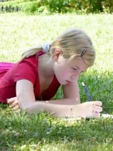 Bambina che scrive a mano sdraiata su un prato