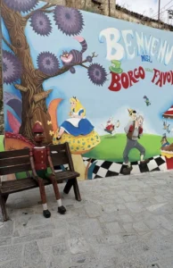 murales alice nel paese delle meraviglie e pinocchio seduto su una panchina