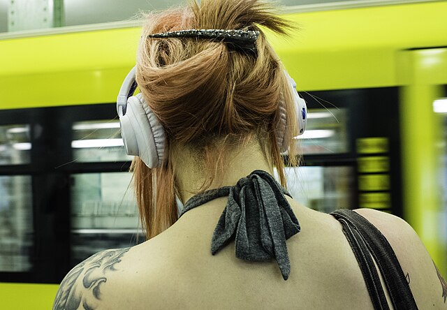 donna di spalle seduta in metro mentre ascolta audiolibri con cuffie