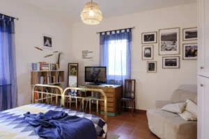 interno della stanza L'amica geniale con tende azzurre ispirate al golfo di Napoli