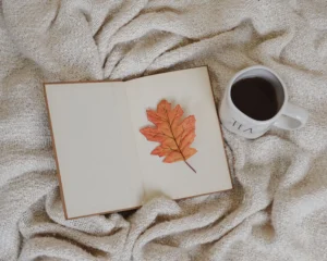 libro aperto con una foglia arancione e una tazza di caffè